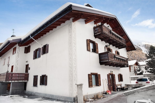 Un immeuble à plusieurs étages doté de balcons en bois, un sol recouvert de neige et un paysage montagneux en arrière-plan.