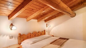 A bedroom with a wooden ceiling, a bed with a headboard, bedside lamps, and a nightstand. - Apartment 'Baita Franz Mansarda 1' with Mountain View, Garden and Wi-Fi (Livigno)
