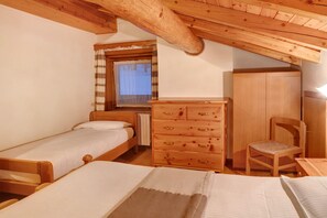 Une chambre avec deux lits simples, une commode en bois, une chaise et une fenêtre avec des rideaux.