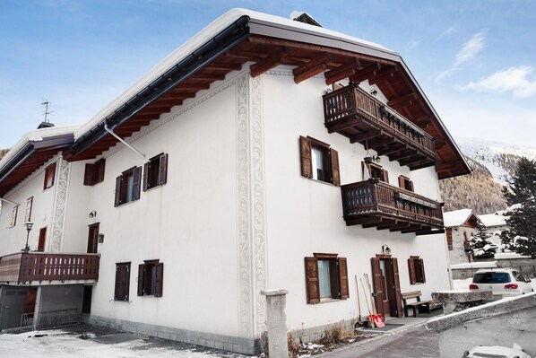 Un immeuble à plusieurs étages doté de balcons en bois, un sol recouvert de neige et un paysage montagneux en arrière-plan.