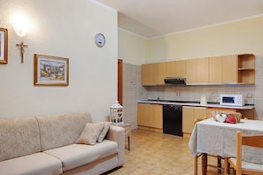 Un salon avec un canapé, une table à manger avec des chaises, une cuisine avec des meubles en bois et un four à micro-ondes, et une horloge murale.