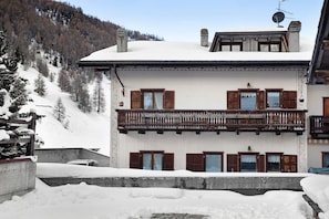 A two-story building with a balcony, snow-covered surroundings, and a mountainous backdrop.