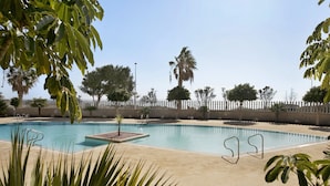 Una piscina con cerca blanca, palmeras y cielo despejado.