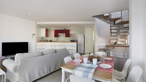 Un espacio habitable moderno con sofá, mesa de comedor, sillas, televisor de pantalla plana, zona de cocina y una escalera.