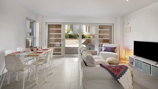 Una sala de estar moderna con sofá, televisor, mesa de comedor, sillas y un balcón con vistas.