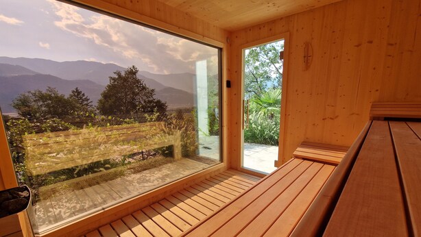 Une pièce en bois avec une grande fenêtre, un banc et une porte donnant sur l’extérieur.