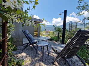 An outdoor seating area with a view of mountains, a concrete structure, and a metal fence.