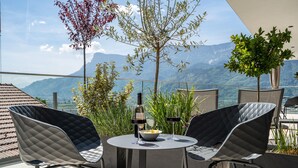 Une terrasse avec deux chaises, une table, une bouteille de vin et un saladier de fruits.
