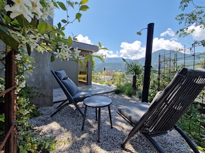 An outdoor seating area with a view of mountains, a concrete structure, and a metal fence.