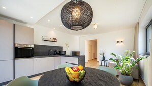 Een moderne keuken met een ronde eettafel, een zwarte kroonluchter en een schaal met fruit.