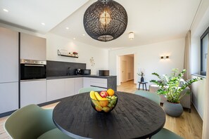 A modern kitchen with a round dining table, a black chandelier, and a bowl of fruit.
