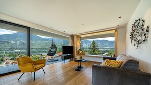 A modern living room with a large window, a sofa, a chair, a TV, and a small table. - Apartment "Videre Penthouse Lodge Exclusive" with Mountain View, Wi-Fi & Terrace (Gargazon)