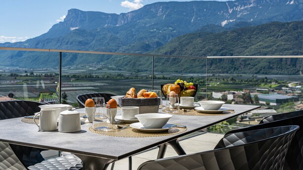 A dining table set with breakfast items and a fruit bowl, overlooking a mountainous landscape. - Apartment "Videre Penthouse Lodge Exclusive" with Mountain View, Wi-Fi & Terrace (Gargazon)