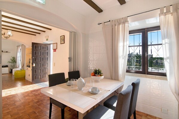 A dining area with a white table, chairs, a teapot, and a bowl of fruit.