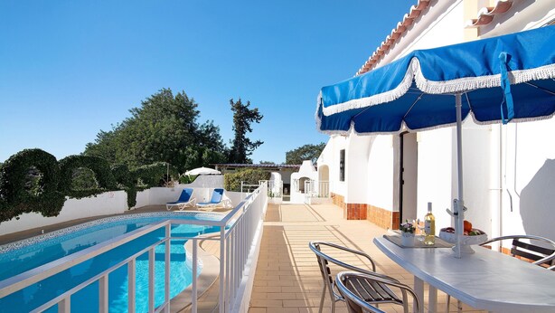 A poolside area with a pool, lounge chairs, a table with a blue umbrella, and a view of the surrounding landscape. - "Vila Caracol" with Pool, Tennis Court, A/C & Wi-Fi (Guia)