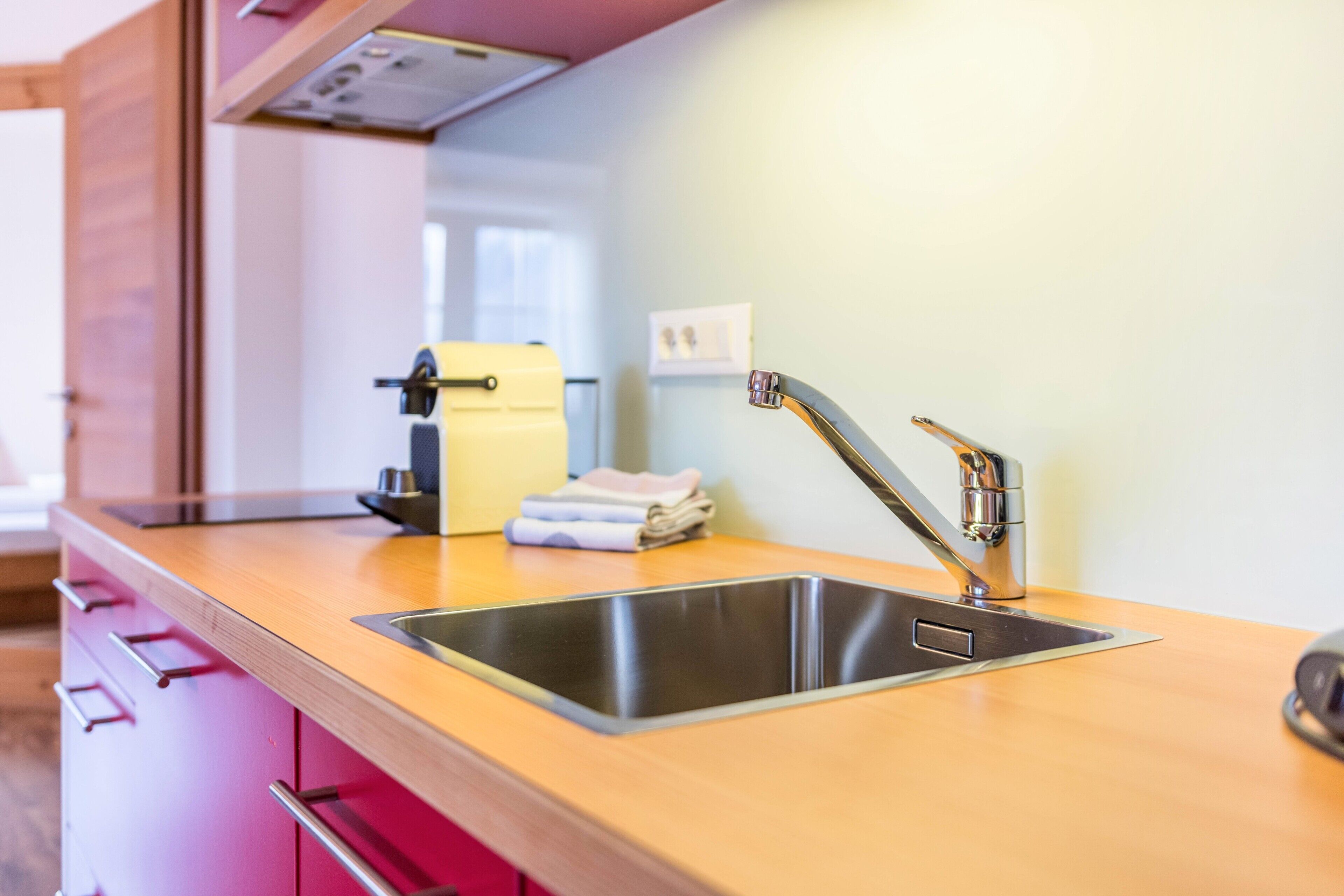 A modern kitchen with a stainless steel sink, wooden countertop, and pink cabinets.