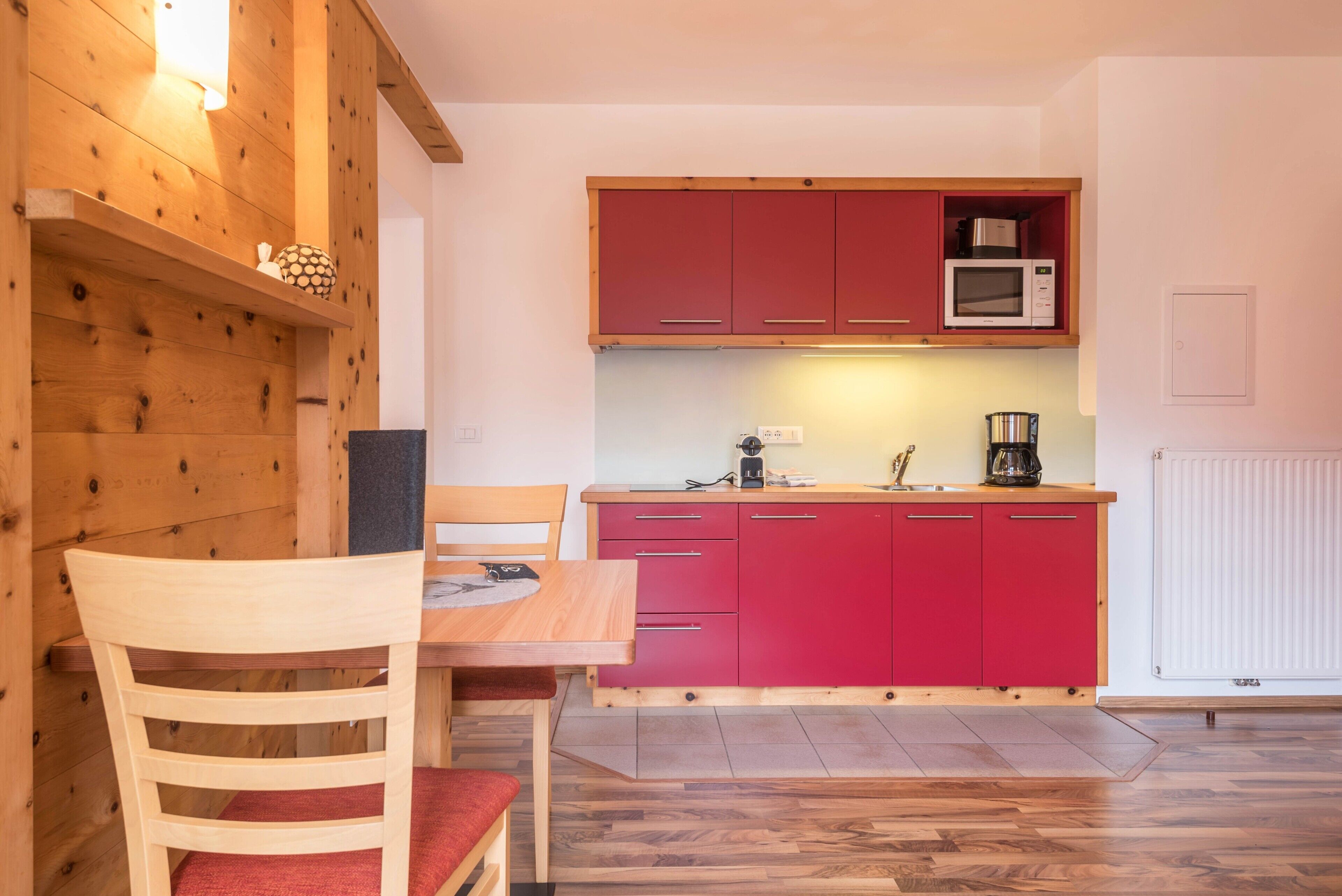 Eine kleine Küche mit einem Holztisch, einem roten Schrank und einer Mikrowelle.