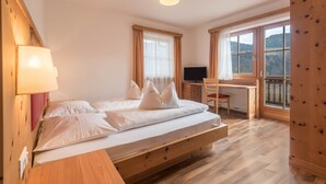 A bedroom with a bed, a desk, a chair, a TV, and a window with a view. - Holiday Apartment 'Riegelehof 1' with Balcony, Garden & Wi-Fi (Lajen)