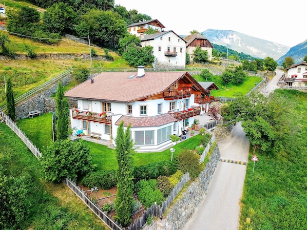 A large house with a balcony, surrounded by greenery and a mountain view.