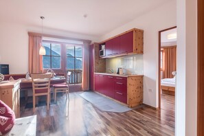 Een compacte keuken met houten kastjes, een magnetron, en een eethoek met een tafel en stoelen.