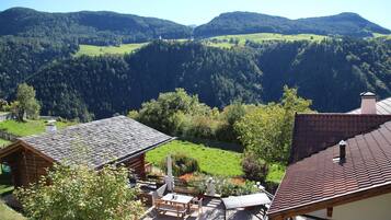 Eine Berghütte mit Terrassenbereich, Holzhütten und Blick auf die umliegenden bewaldeten Hügel.