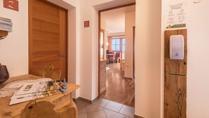 Un couloir d’hôtel avec des portes en bois, des panneaux indiquant les numéros de chambre, un coin repas avec une table et des chaises, et une vue sur la chambre.