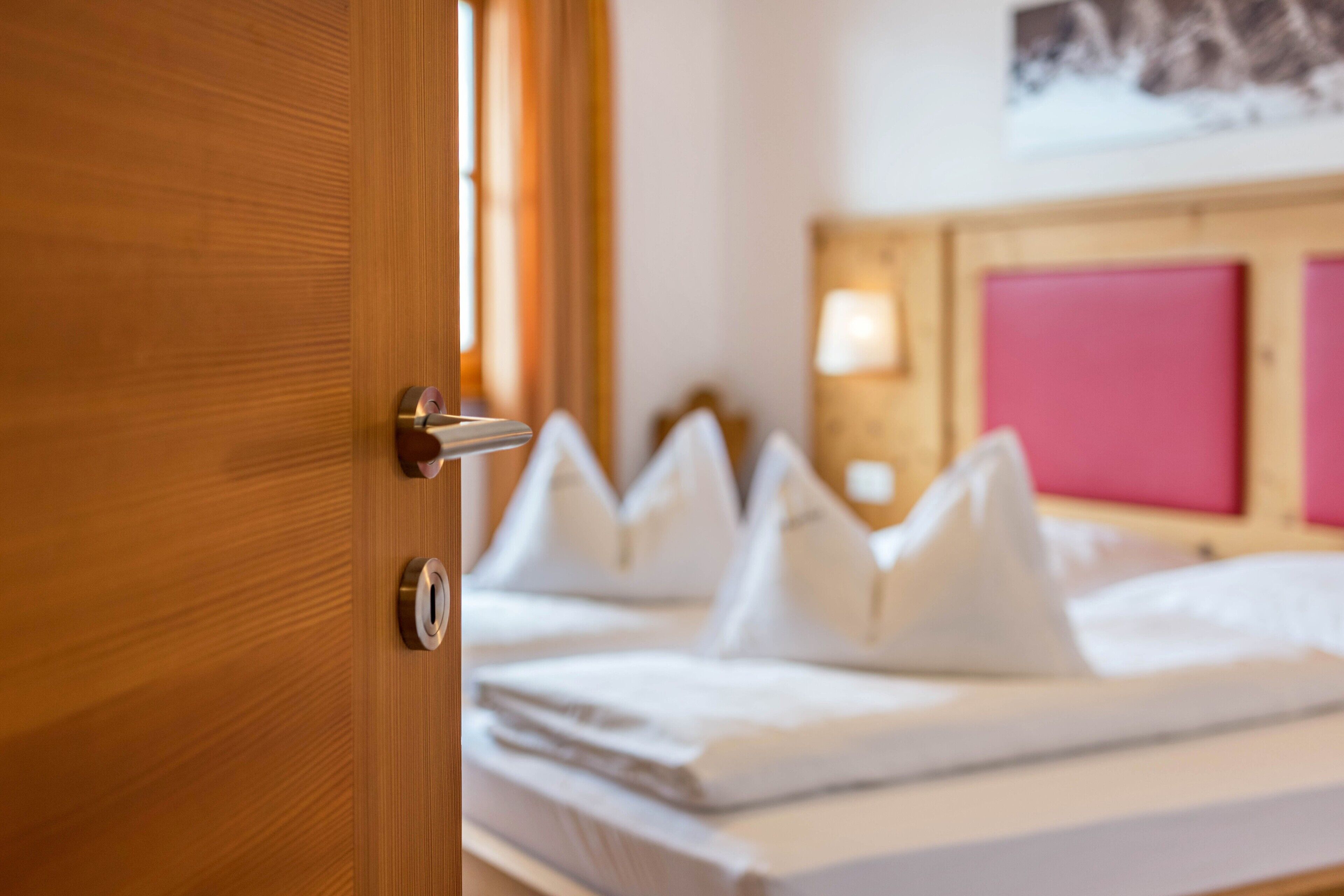 A hotel room with a wooden door, a bed with white bedding, and a pink headboard.