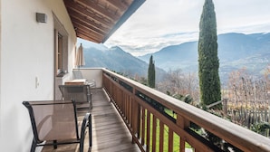 Un balcon doté d’une balustrade en bois, d’une chaise, d’une table et offrant une vue sur les montagnes.