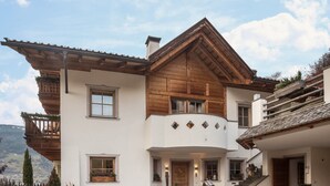 Un bâtiment à deux étages doté d’une façade en bois, d’un balcon et d’un escalier en pierre menant à l’entrée.