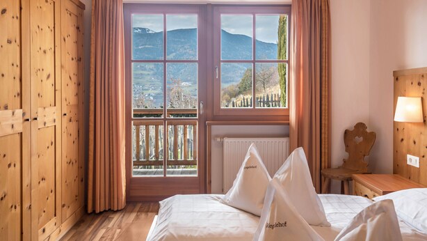 Une chambre avec un lit, une armoire en bois et une fenêtre donnant sur les montagnes.