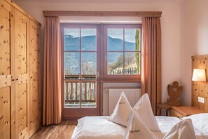 Una habitación con cama, armario de madera y ventana con vistas a montañas.