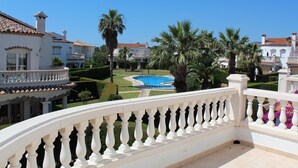 A pool surrounded by manicured gardens and white buildings with red-tiled roofs.