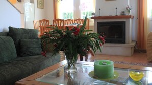 A living room with a sofa, a glass coffee table, a green candle, a fireplace, and a dining area with chairs and a table.