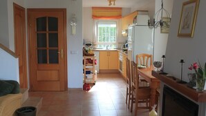 A kitchen with a dining table, chairs, a refrigerator, and a window with curtains.