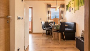 A modern kitchen with wooden cabinets, a dining area with a black sofa and chairs, and a view of the outdoors through a window. - Apartment 'Kehrerhof - Mountain' with Mountain View, Balcony & Wi-Fi (St. Lorenzen)