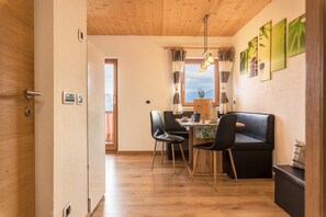 Une cuisine moderne avec des meubles en bois, un coin repas avec un canapé et des chaises noirs, et une vue sur l’extérieur par une fenêtre.