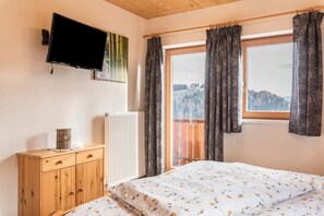 Une chambre à coucher comprenant un lit, une commode, un téléviseur, une fenêtre avec des rideaux et une vue sur une montagne.