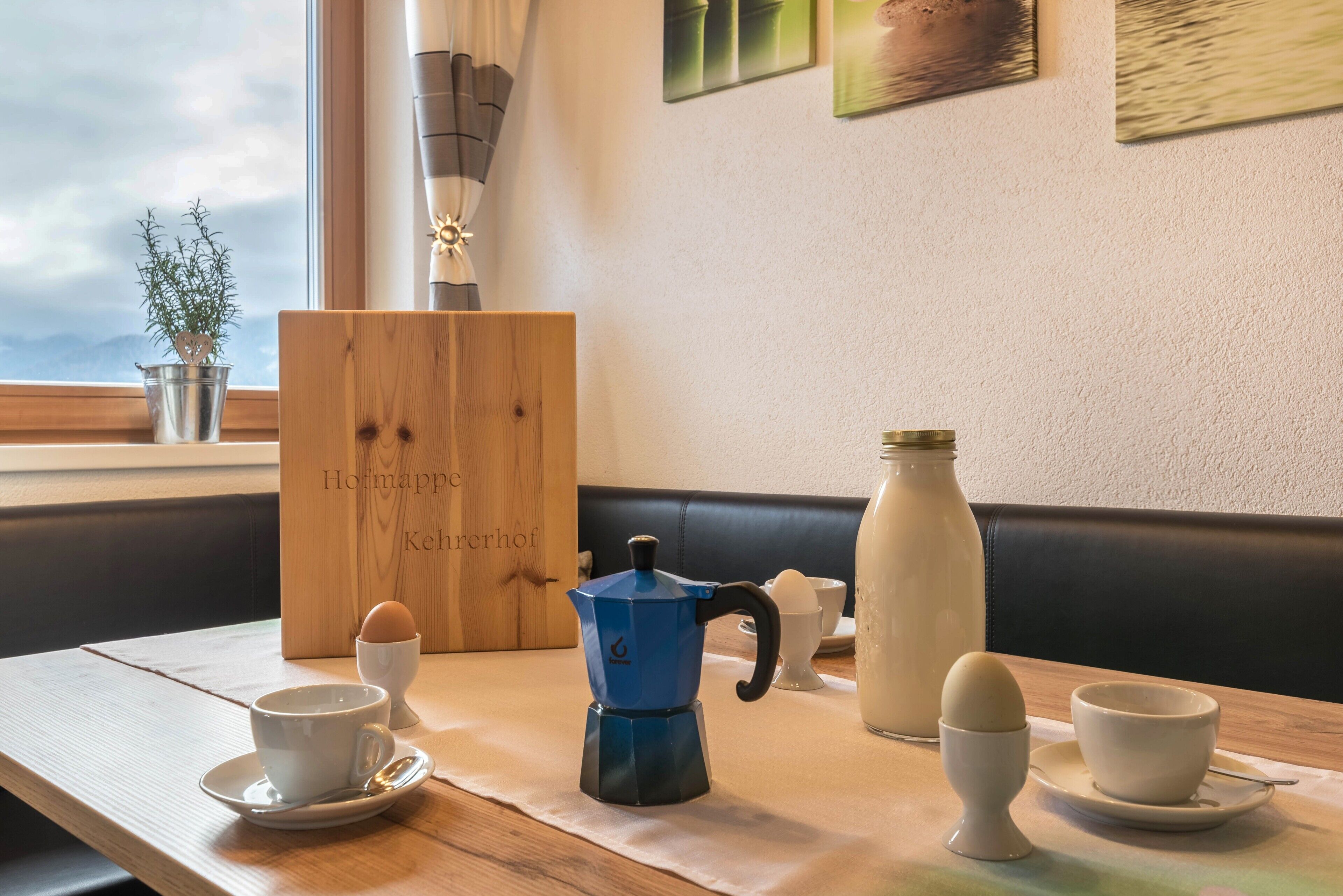 Ein Esstisch mit Kaffeemaschine, Eiern und einer Flasche, vor einem Fenster mit Blick.