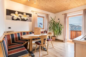 Un espace repas avec une table en bois, des bancs, une plante en pot et une vue sur l’extérieur.