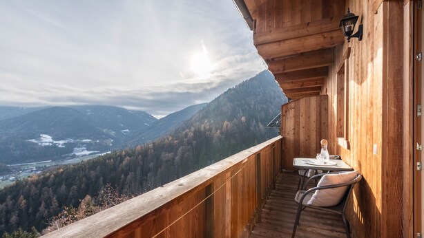 Ein Holzbalkon mit Tisch und Stühlen mit Blick auf eine gebirgige Landschaft.