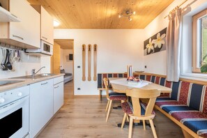 Una cocina compacta con electrodomésticos blancos, una mesa de madera con bancos y vistas al exterior.