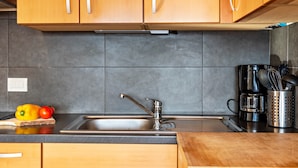 A kitchen with wooden cabinets, a stainless steel sink, a coffee maker, and a cutting board with vegetables. - Apartment 'Kehrerhof - Panorama' with Mountain View, Balcony & Wi-Fi (St. Lorenzen)