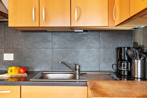 A kitchen with wooden cabinets, a stainless steel sink, a coffee maker, and a cutting board with vegetables.