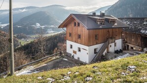 A wooden house with a white lower section, a staircase, and a view of a valley and mountains. - Apartment 'Kehrerhof - Panorama' with Mountain View, Balcony & Wi-Fi (St. Lorenzen)