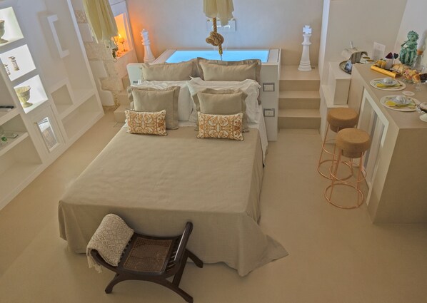 A bedroom with a bed, bedside tables, a chair, a desk with stools, and a small balcony.