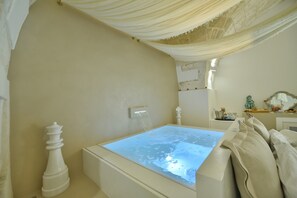 A room with a large, illuminated water feature in the center, a white decorative object on the left, and a white cabinet with a mirror and small items on the right.