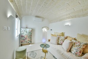 Un salon avec un canapé blanc, des coussins à motifs, une table basse en verre et une sculpture d’animal décorative.