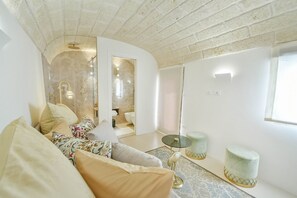A living room with a curved ceiling, a sofa, a glass door leading to a bathroom, and two round tables.