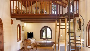 A spacious room with a high ceiling, a wooden staircase, a dining area with a table and chairs, and a television. - Country House "Finca Los Dioses" in the Heart of Nature with Mountain View, Garden & Terrace (Mogán)