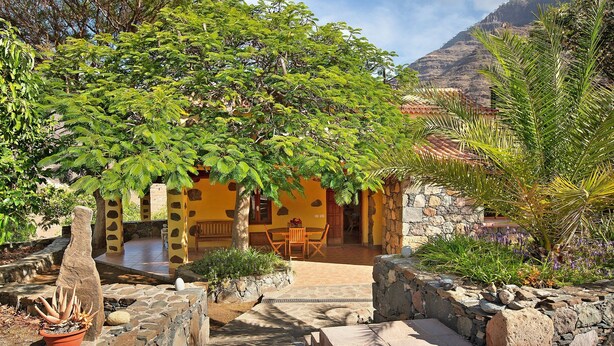 A courtyard with a stone pathway, a cactus planter, and a yellow building with a tiled roof. - Country House "Finca Los Dioses" in the Heart of Nature with Mountain View, Garden & Terrace (Mogán)